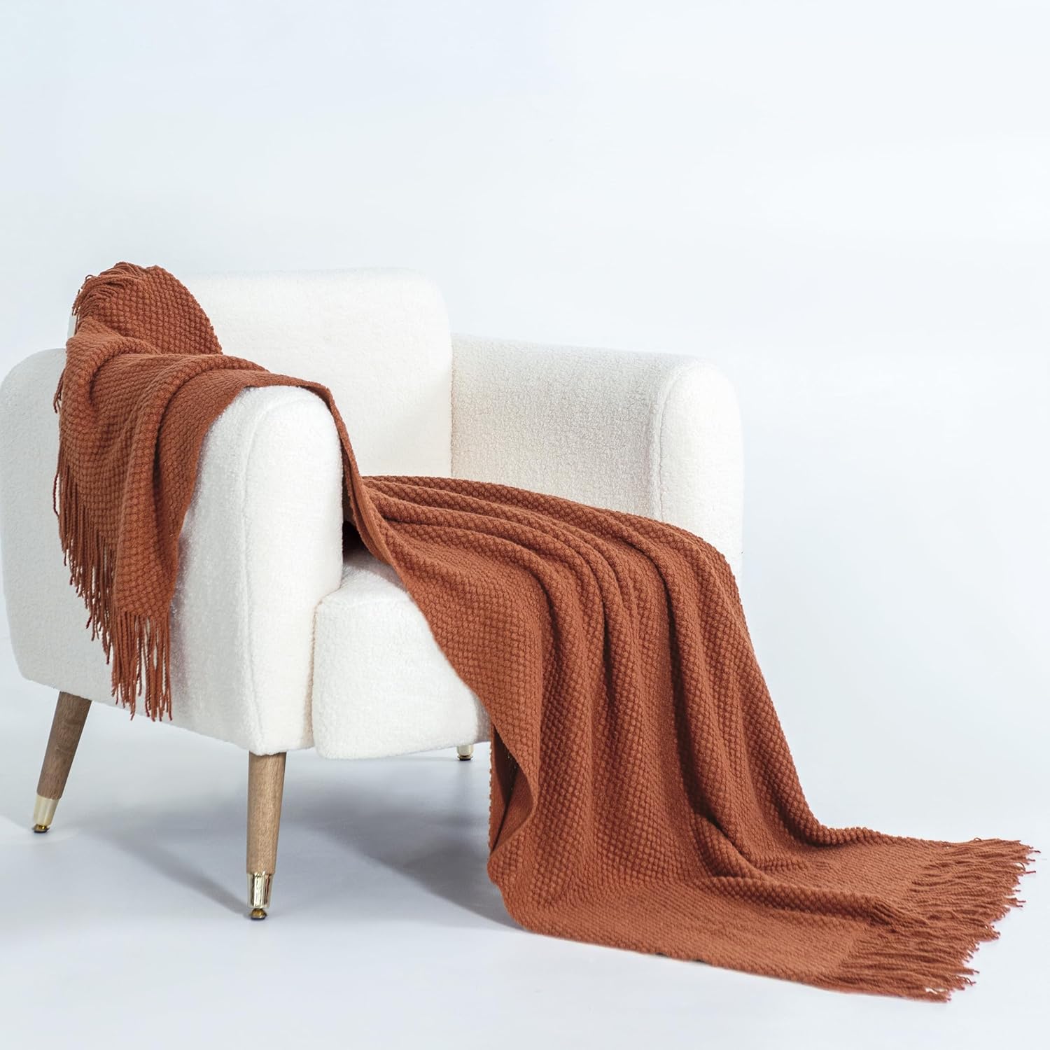 Terracotta micro plush knitted throw blanket draped over a white armchair, showcasing its cozy and elegant texture.