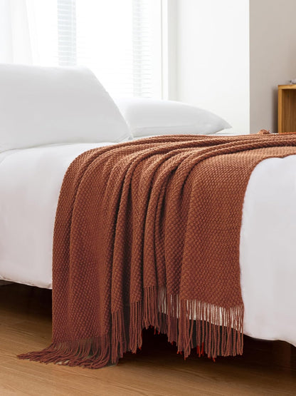 Terracotta micro plush throw blanket draped over a bed, showcasing its knitted woven design and cozy, elegant appearance.