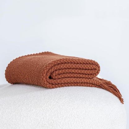 Terracotta micro plush knitted woven throw blanket on a white surface, showcasing its soft and cozy texture.