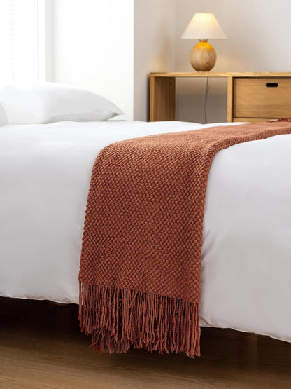 Terracotta micro plush knitted throw blanket draped on a bed, showcasing its soft texture and elegant design.