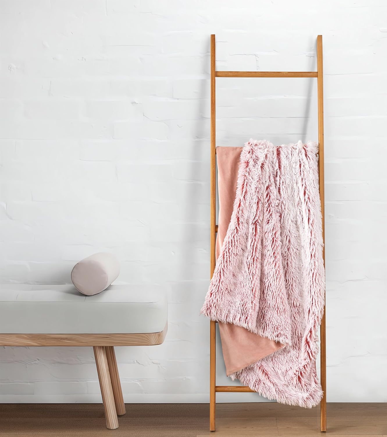 Rose faux fur throw blanket hanging on wooden ladder, showcasing plush texture and reversible design for luxurious home comfort.