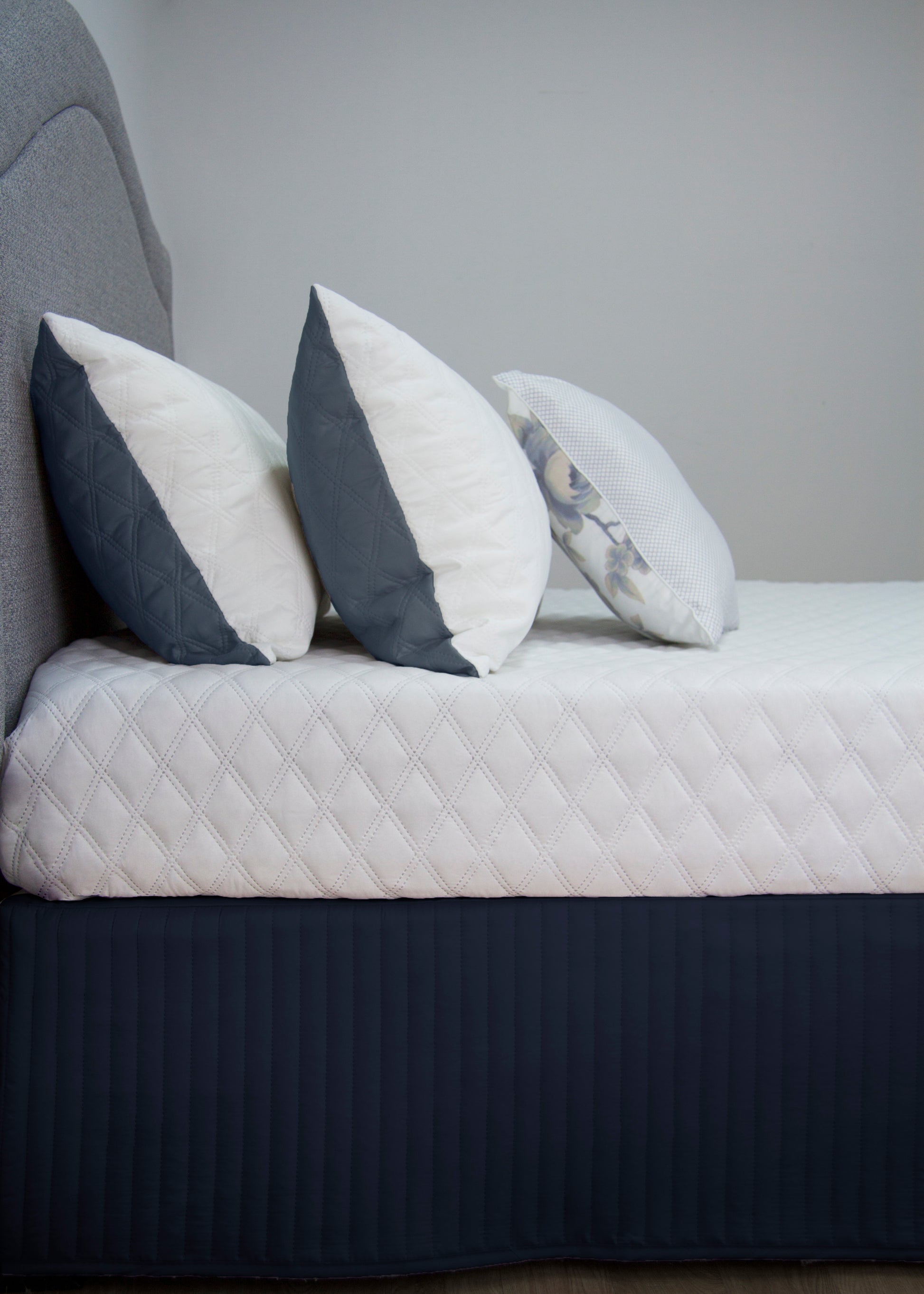 Quilted navy bedskirt valance with decorative pillows, enhancing elegant bedroom décor.