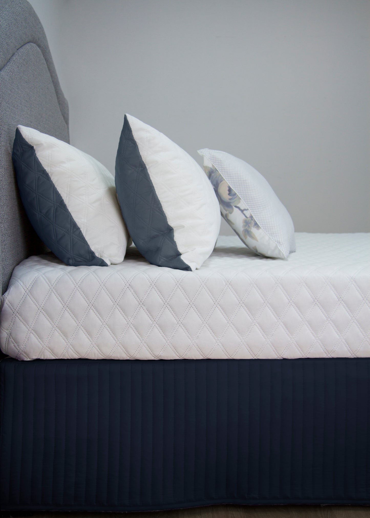 Quilted navy bedskirt valance with decorative pillows on a queen size bed, enhancing elegant bedroom décor.