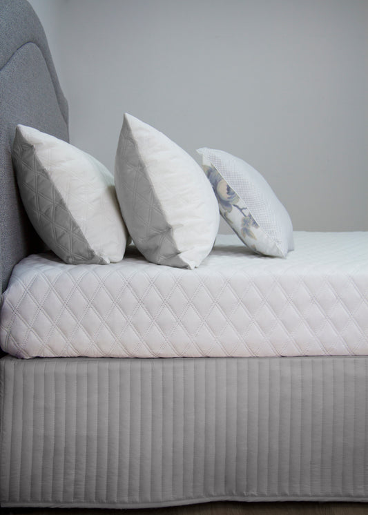 Elegant quilted bedskirt valance with white decorative pillows on a stylish bed, perfect for chic bedroom décor.