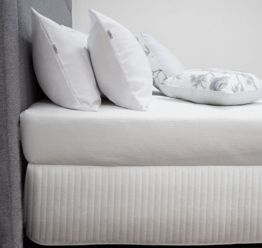 Elegant quilted white bed skirt with decorative pillows, enhancing a queen size bed's stylish look.