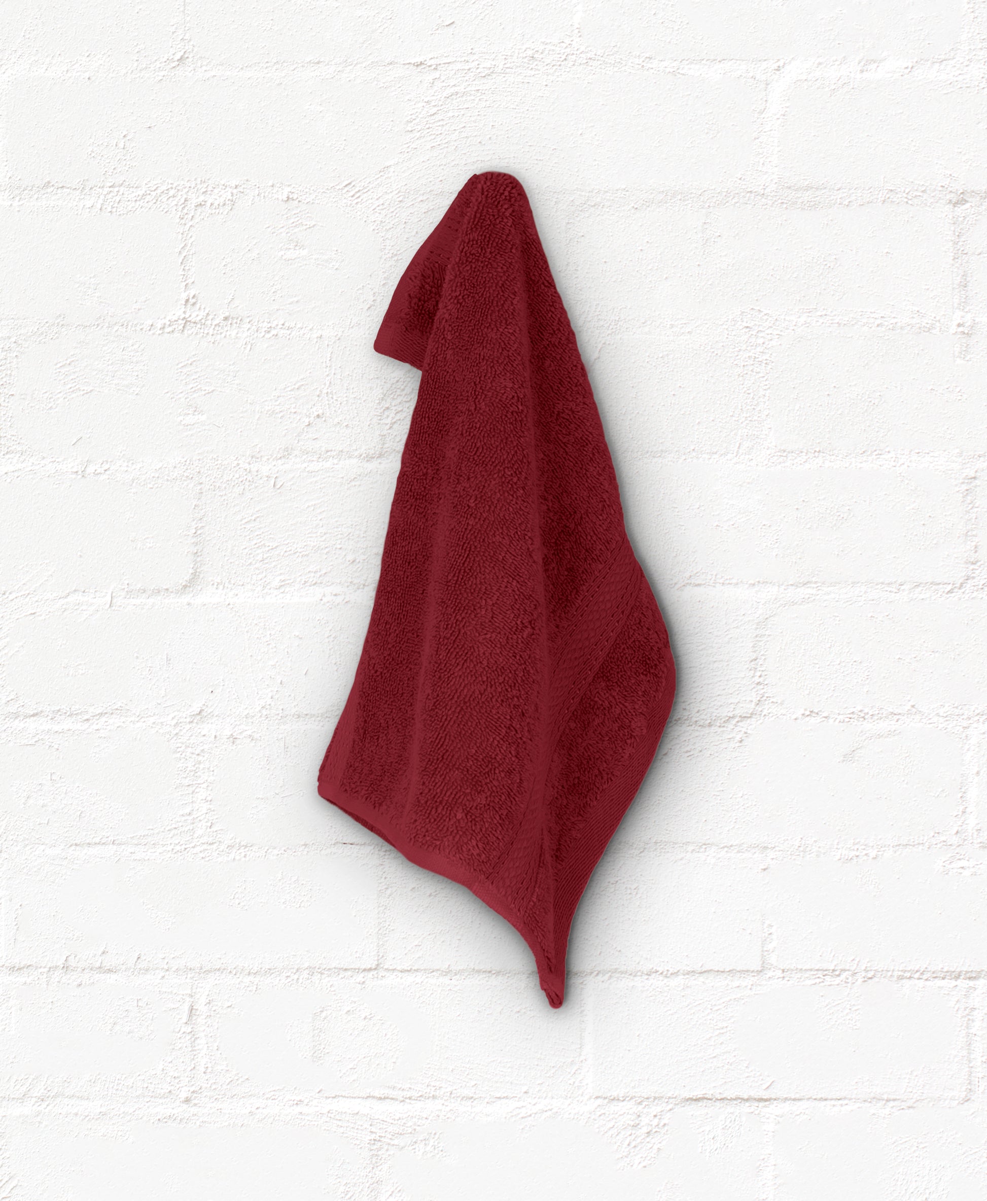 Burgundy cotton bath towel hanging on white wall, part of St. Regis 7-piece luxury bathroom towel set.