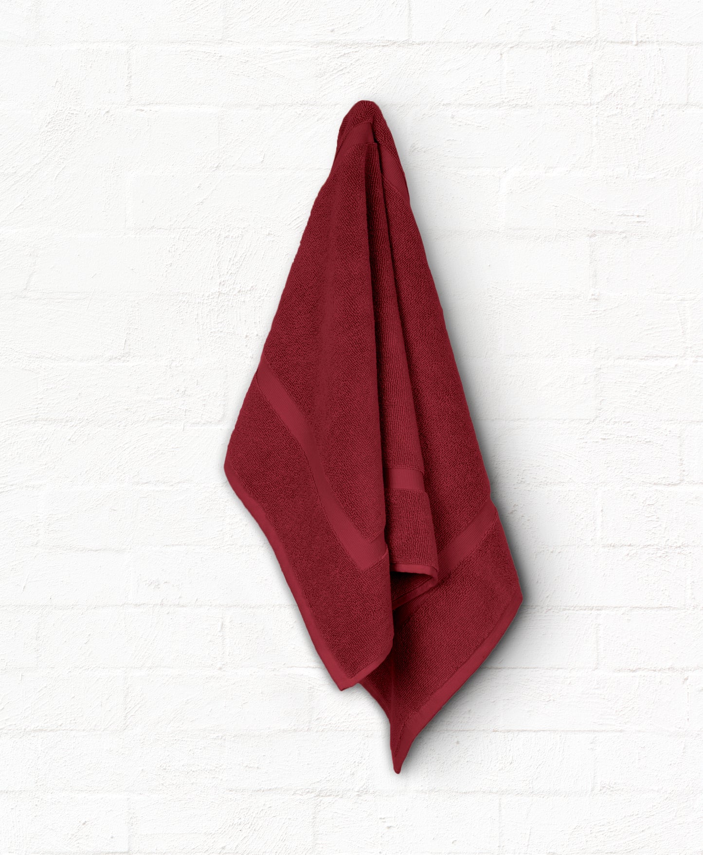 Burgundy cotton luxury bath towel hanging on white wall from St. Regis 7-piece bathroom towel set.