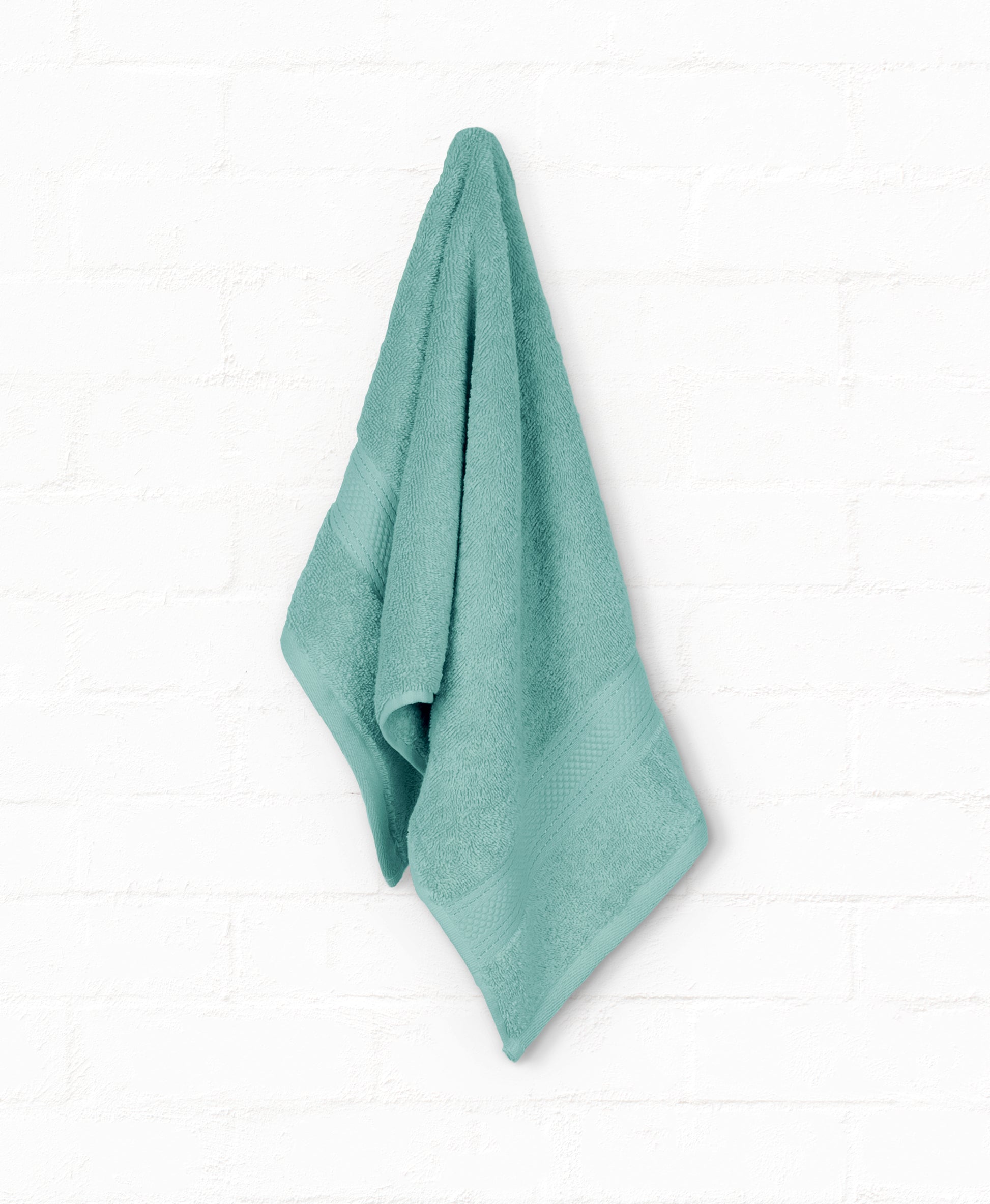 Teal cotton bath towel from St. Regis 7-piece luxury collection hanging on white wall.