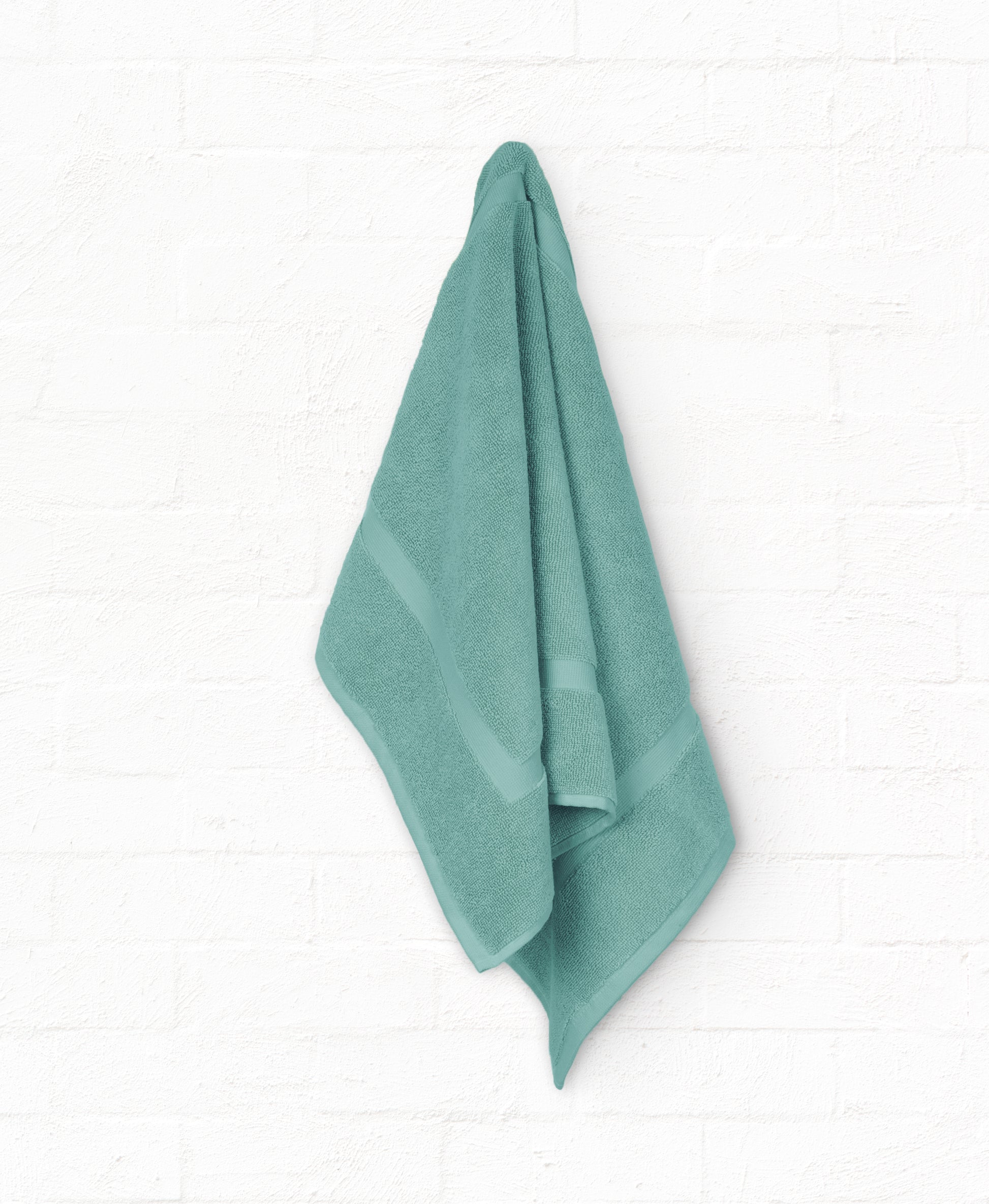 Luxury teal cotton bath towel hanging on white wall, part of a 7-piece St. Regis bathroom towel set, made from 100% cotton.