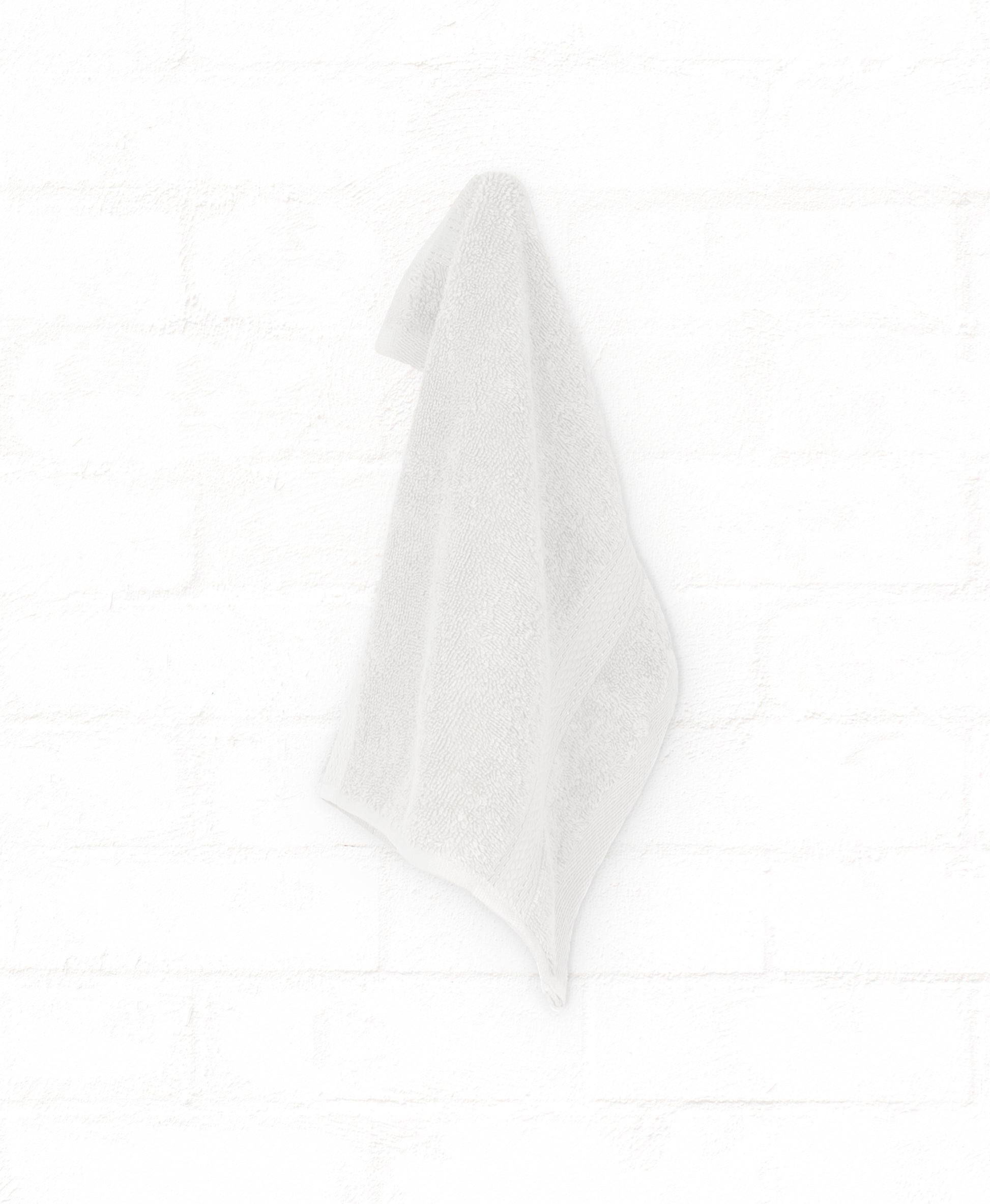 White cotton bath towel from the St. Regis 7-piece luxury collection hanging against a white brick wall.