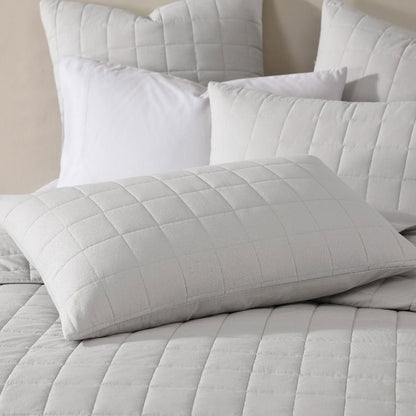 Contemporary silver oblong cushion with quilted cover on a bed, surrounded by soft white pillows.