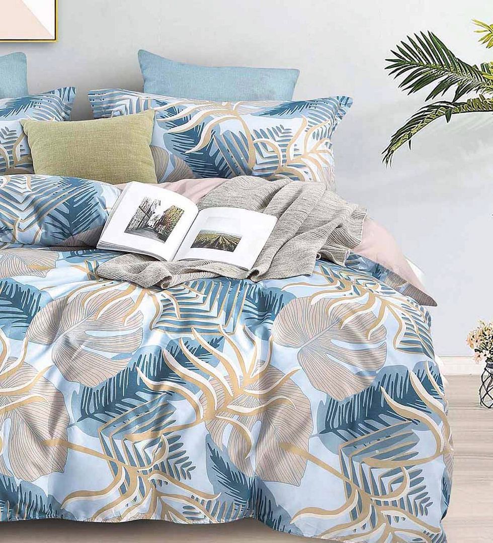 Elegant blue and beige quilt cover set with tropical leaf pattern, styled with cushions and a cozy throw on a bed.