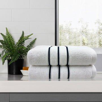 White bath towels with stripes on bathroom counter next to plant