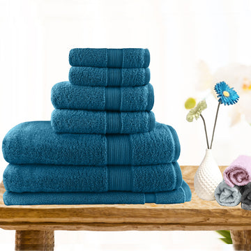 7pc teal cotton bath towel set displayed on a wooden table with decorative flowers, showcasing absorbent and lightweight towels.