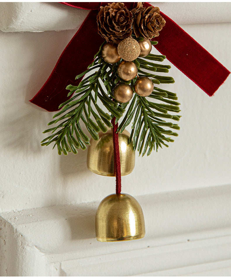 Christmas door ornament with pinecones, golden bells, and red velvet bow for festive decorations.