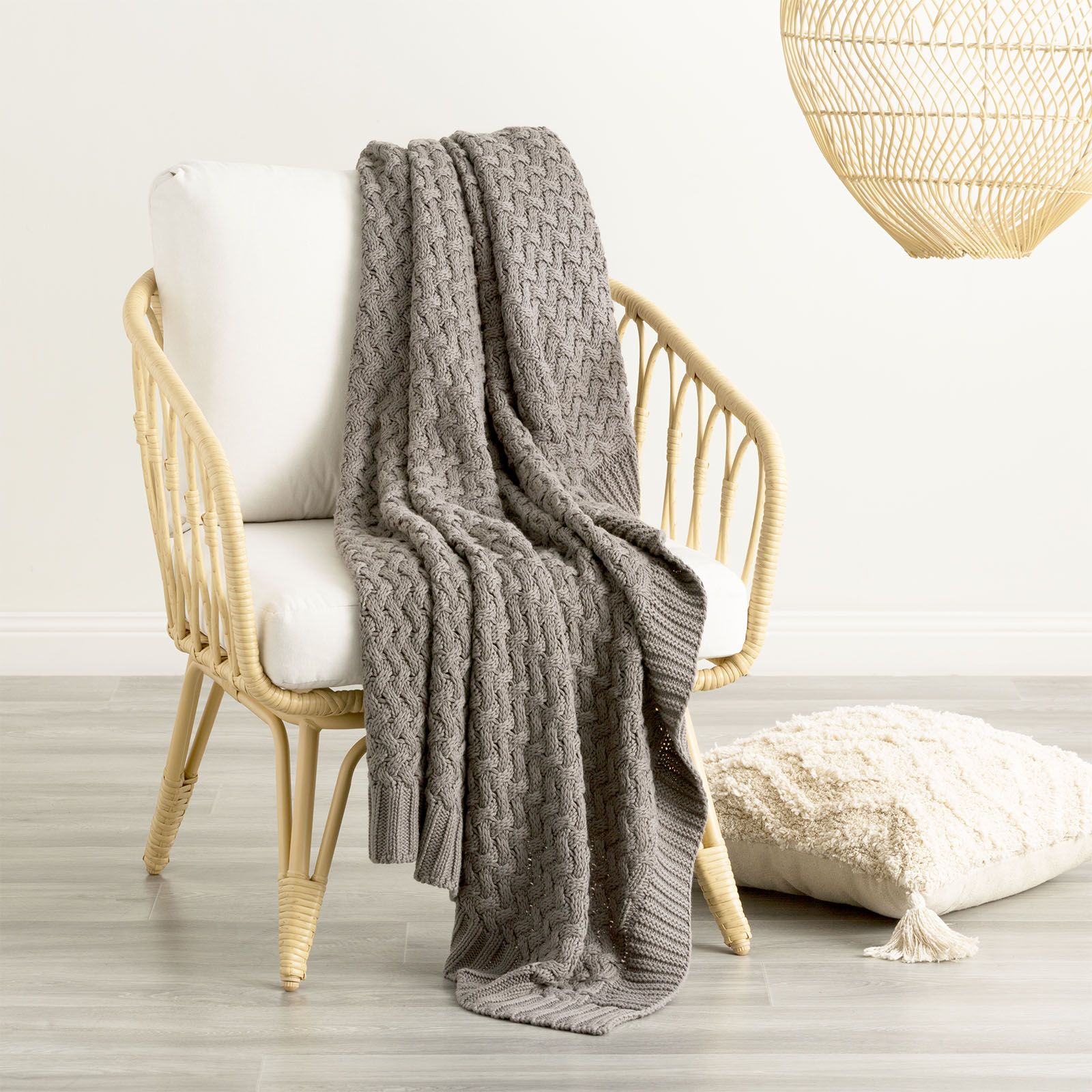 Charcoal Lenni 100% Cotton Knitted Throw Blanket by Renee Taylor draped over a chair, showcasing its chunky knit texture and ribbed edges.