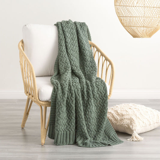 Forest green chunky knit throw blanket draped over a chair, adding warmth and style to a modern room with light decor.