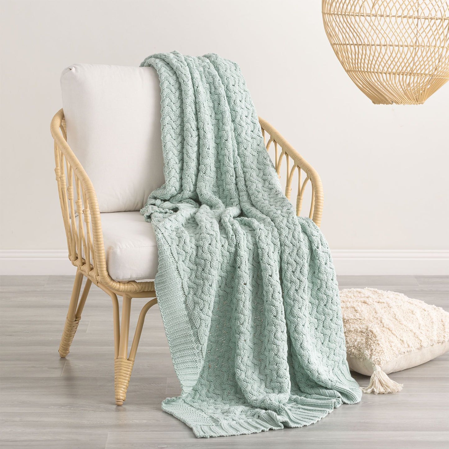 Soft mint green chunky knit throw blanket draped over a chair, featuring a rib knit edge, adding warmth and charm to any room decor.