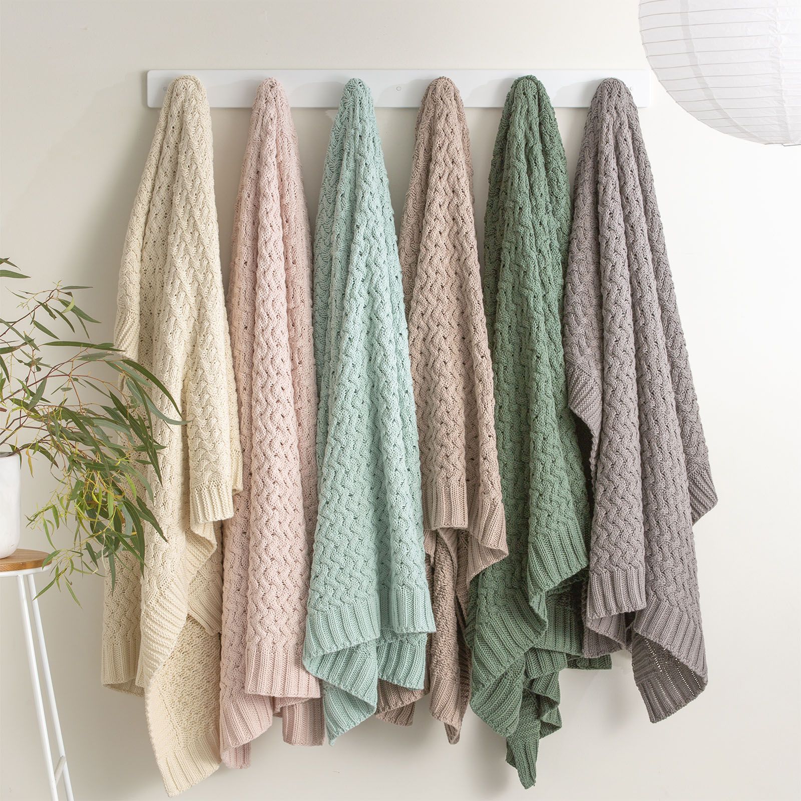 Various colored chunky knit throws hanging on a rack, showcasing the plush, textured design and rib knit edge of the Lenni cotton throws.