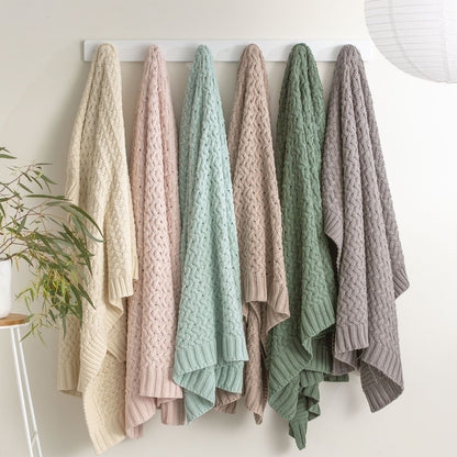 Various colored chunky knit throws hanging on a rack, showcasing the plush, textured design and rib knit edge of the Lenni cotton throws.