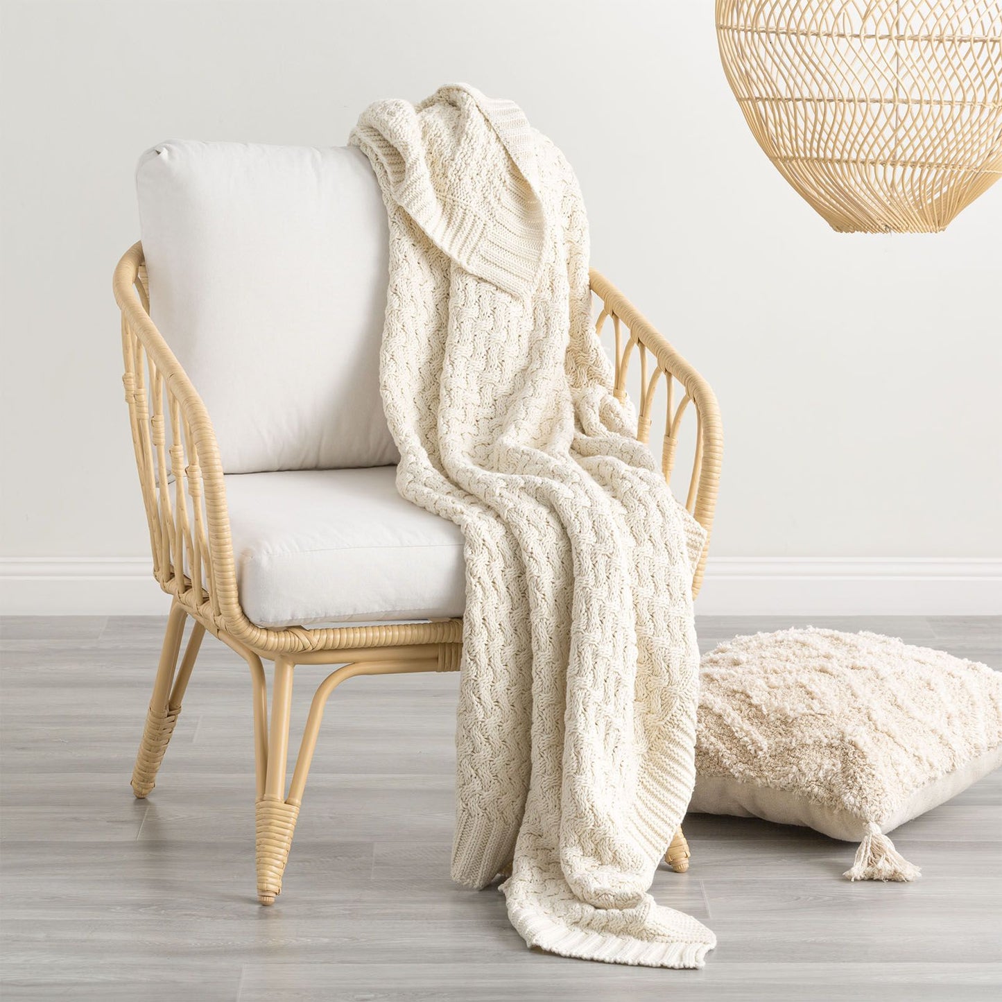 Cream chunky knit throw blanket on rattan chair, cozy home decor accessory.